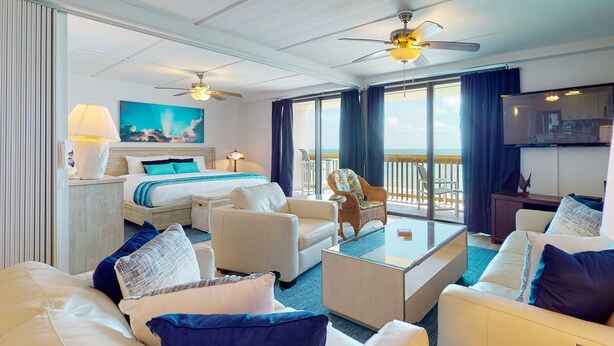 Une chambre d’hôtel comprenant un lit, deux canapés, une table basse, une télévision et un balcon avec vue sur l’océan.