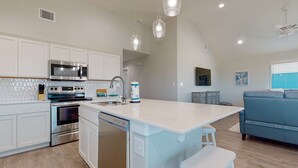 Una cocina moderna con armarios blancos, electrodomésticos de acero inoxidable e iluminación colgante.