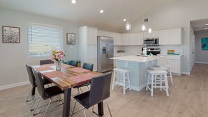 Una cocina moderna con armarios blancos, electrodomésticos de acero inoxidable y una isla central con taburetes.