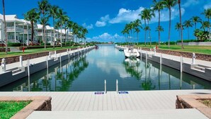Un port de plaisance avec un long canal étroit bordé de palmiers et une rangée de bâtiments blancs dotés de balcons.