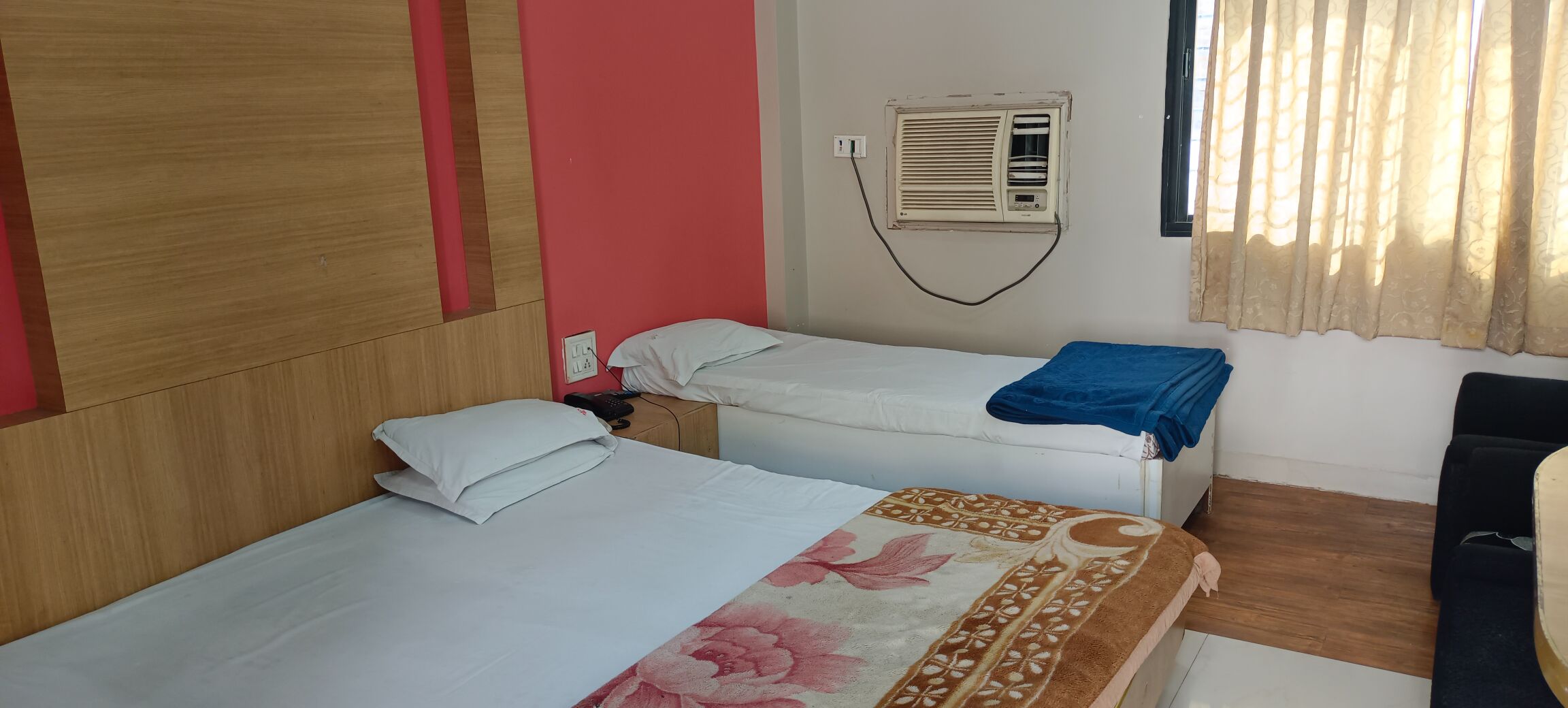 A hotel room with two beds, a wooden headboard, a wall-mounted air conditioner, and a window with curtains.
