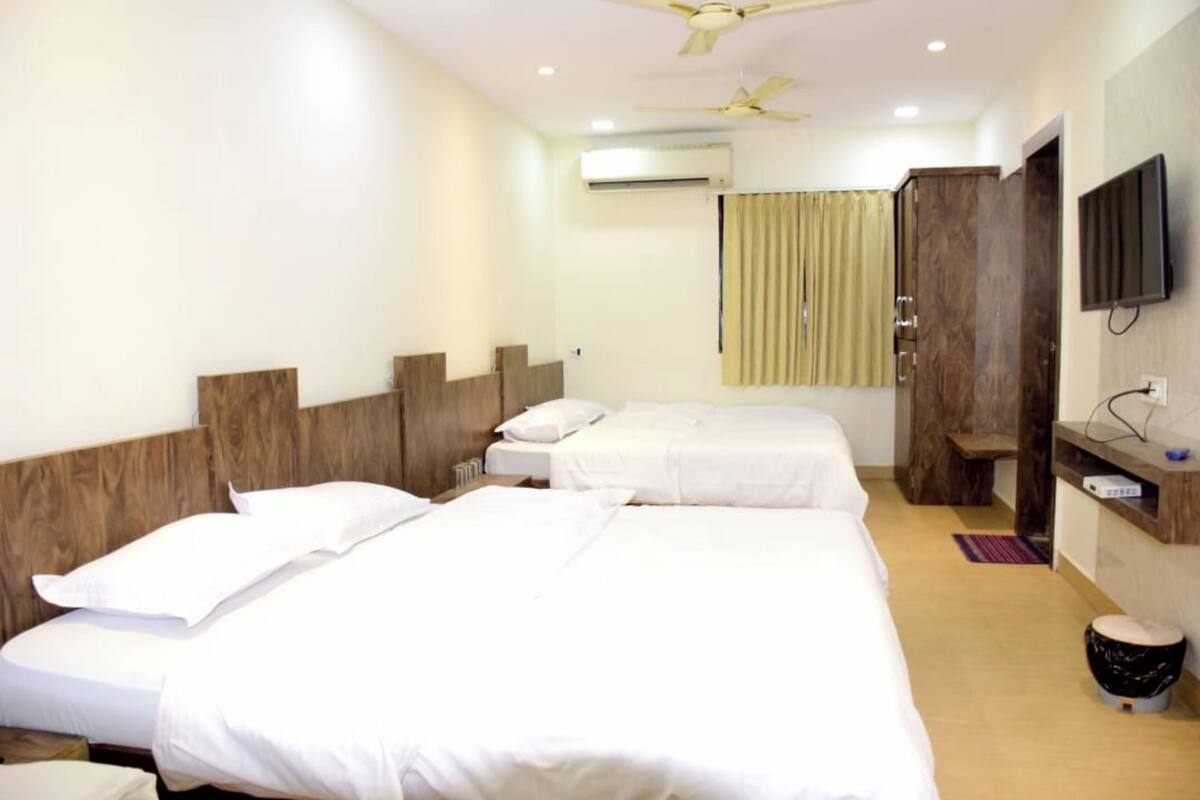 Habitación de hotel con dos camas, televisor, armario y aire acondicionado.