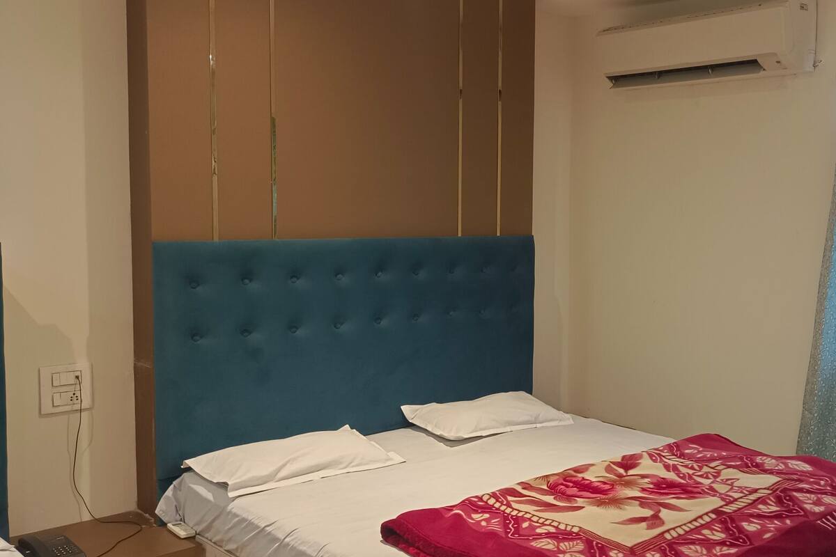 Un dormitorio con cabecera azul, ropa de cama blanca y una manta de cuadros rojos.
