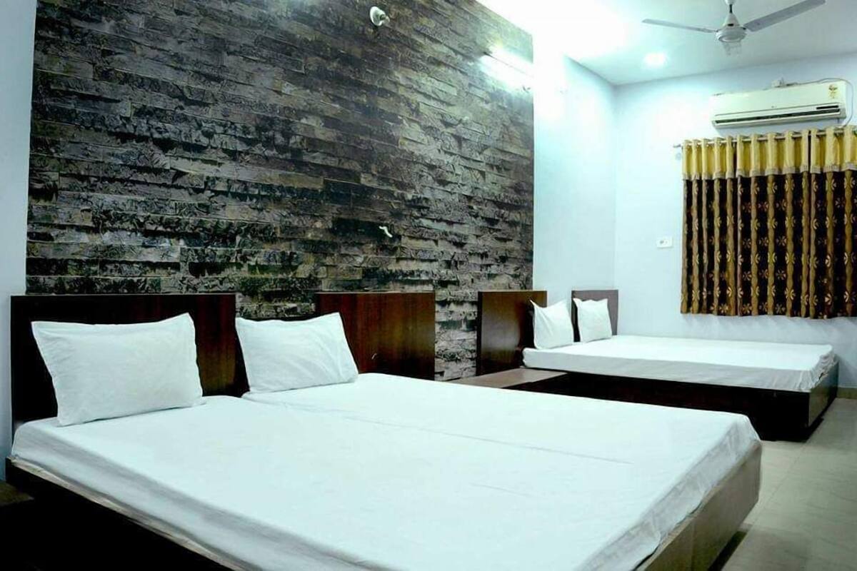 Habitación de hotel con dos camas individuales, un panel de madera decorativo, un equipo de aire acondicionado y una cortina con estampado floral.