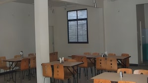 A classroom with tables and chairs, a large window, and ceiling fans. - Hotel Kanha Ujjain (Ujjain)