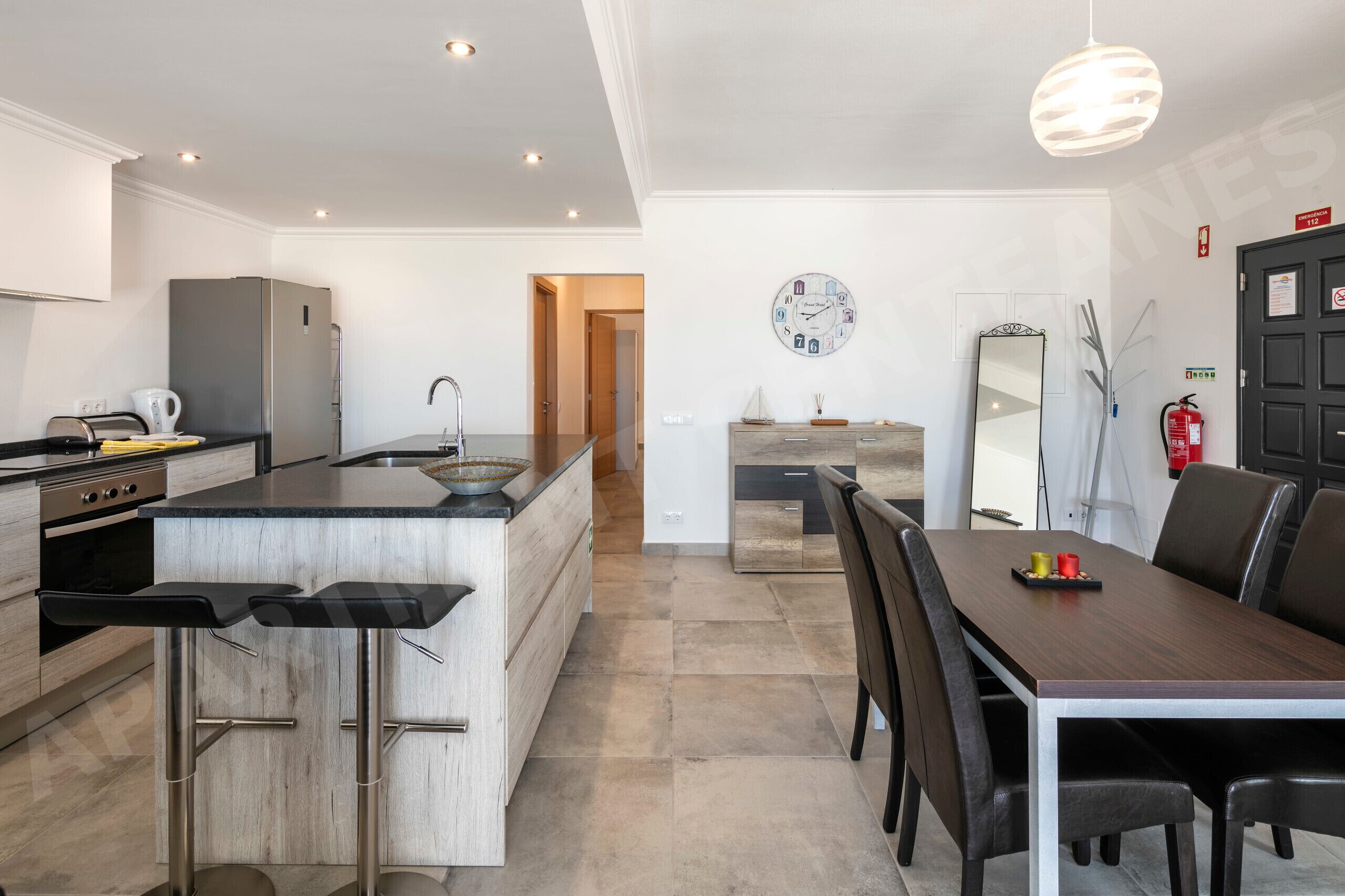 Una cocina moderna con una isla central, taburetes de bar, una mesa de comedor con sillas y un espejo grande.