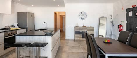 Una cocina moderna con una isla central, taburetes de bar, una mesa de comedor con sillas y un espejo grande.