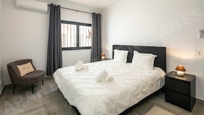 Un dormitorio moderno con una cama grande, una silla, una mesita de noche y un equipo de aire acondicionado.