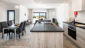 Una cocina moderna con una isla central, comedor con sillas y vistas al exterior.