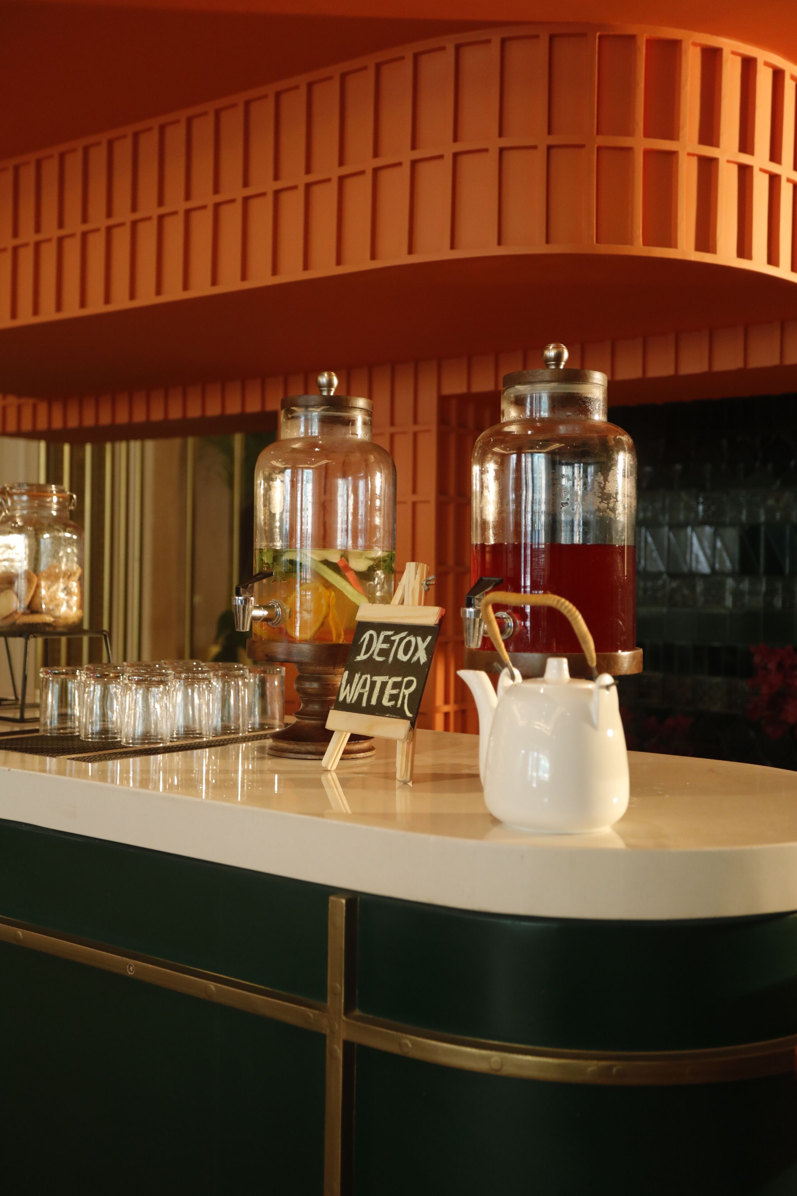 A bar area with a water dispenser, a teapot, and a sign that reads 'DETOX WATER'.