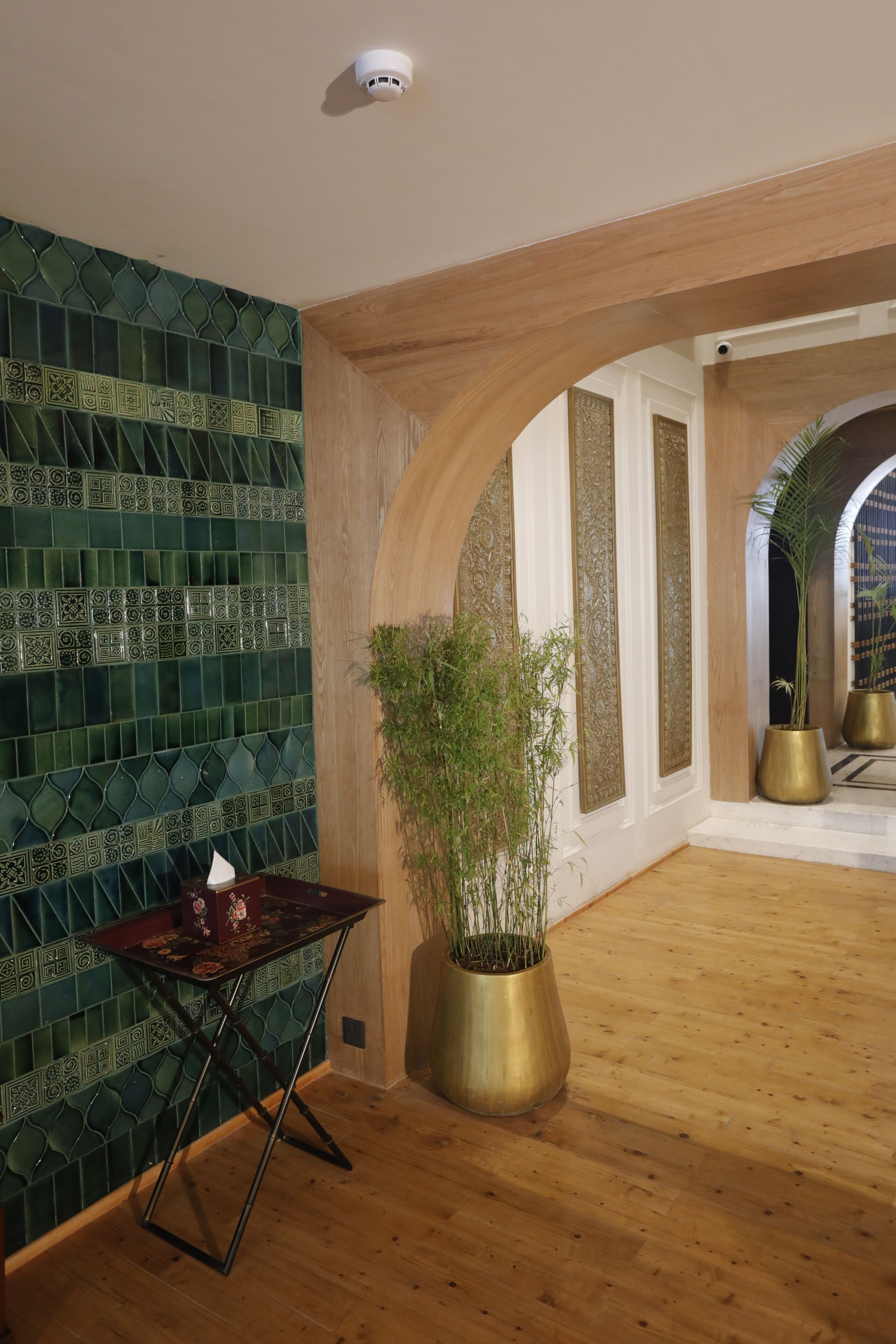 Quarto com parede azulejada, piso de madeira, uma mesa com uma planta e uma porta em arco.