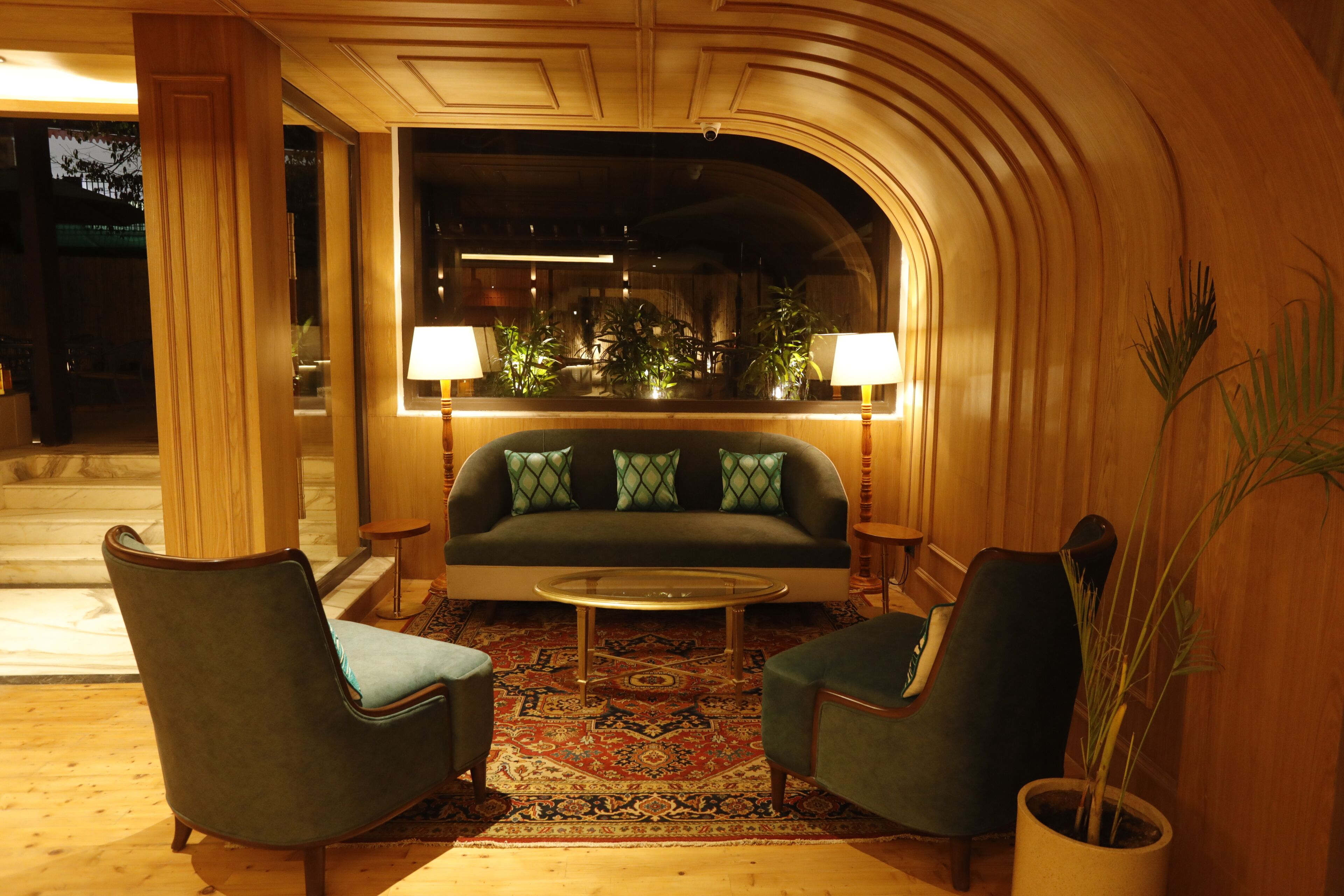 En foyer med sofa, to lænestole, sofabord og et stort spejl der reflekterer rummet.