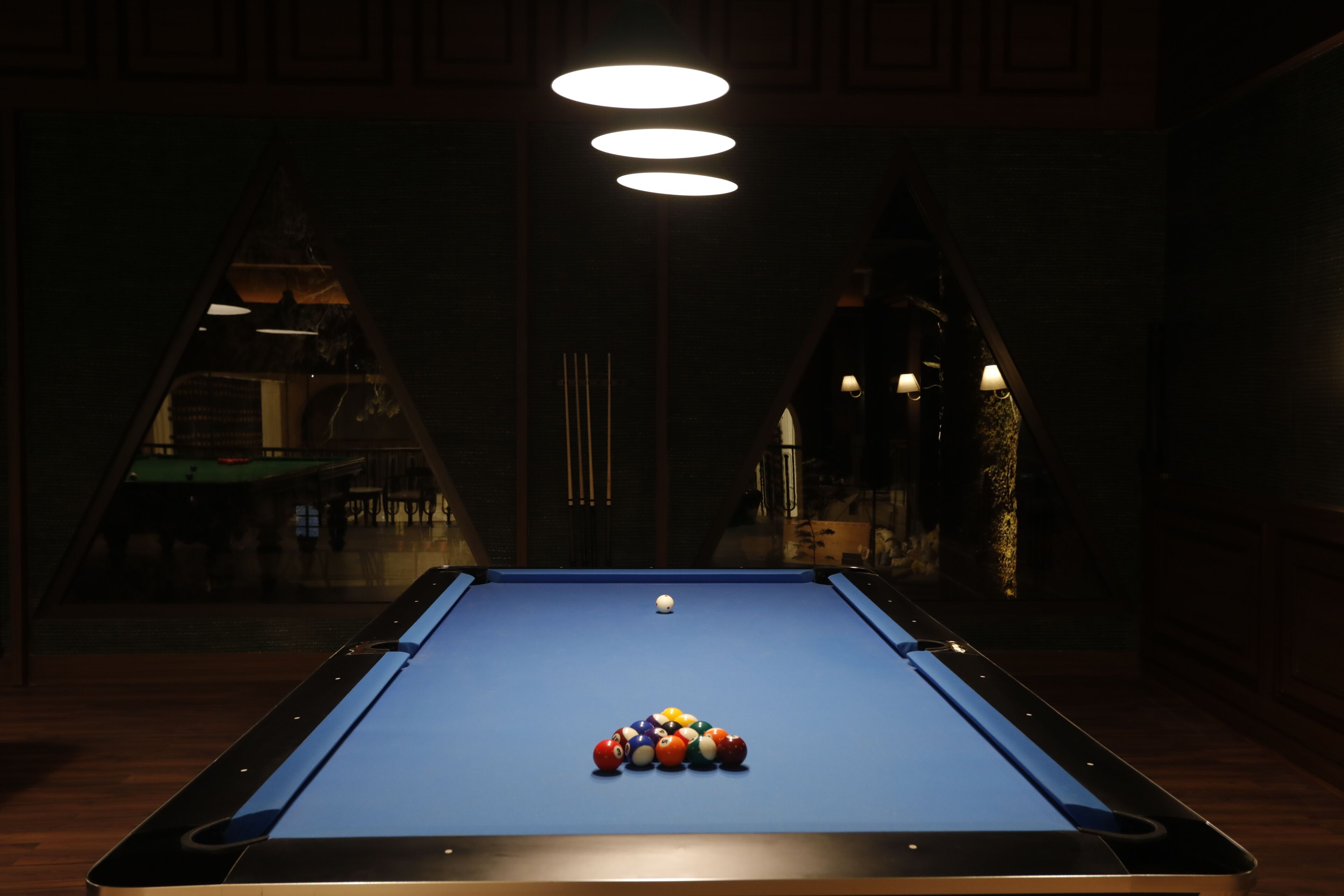 A pool table with balls in the center, surrounded by dark walls and a visible archway.