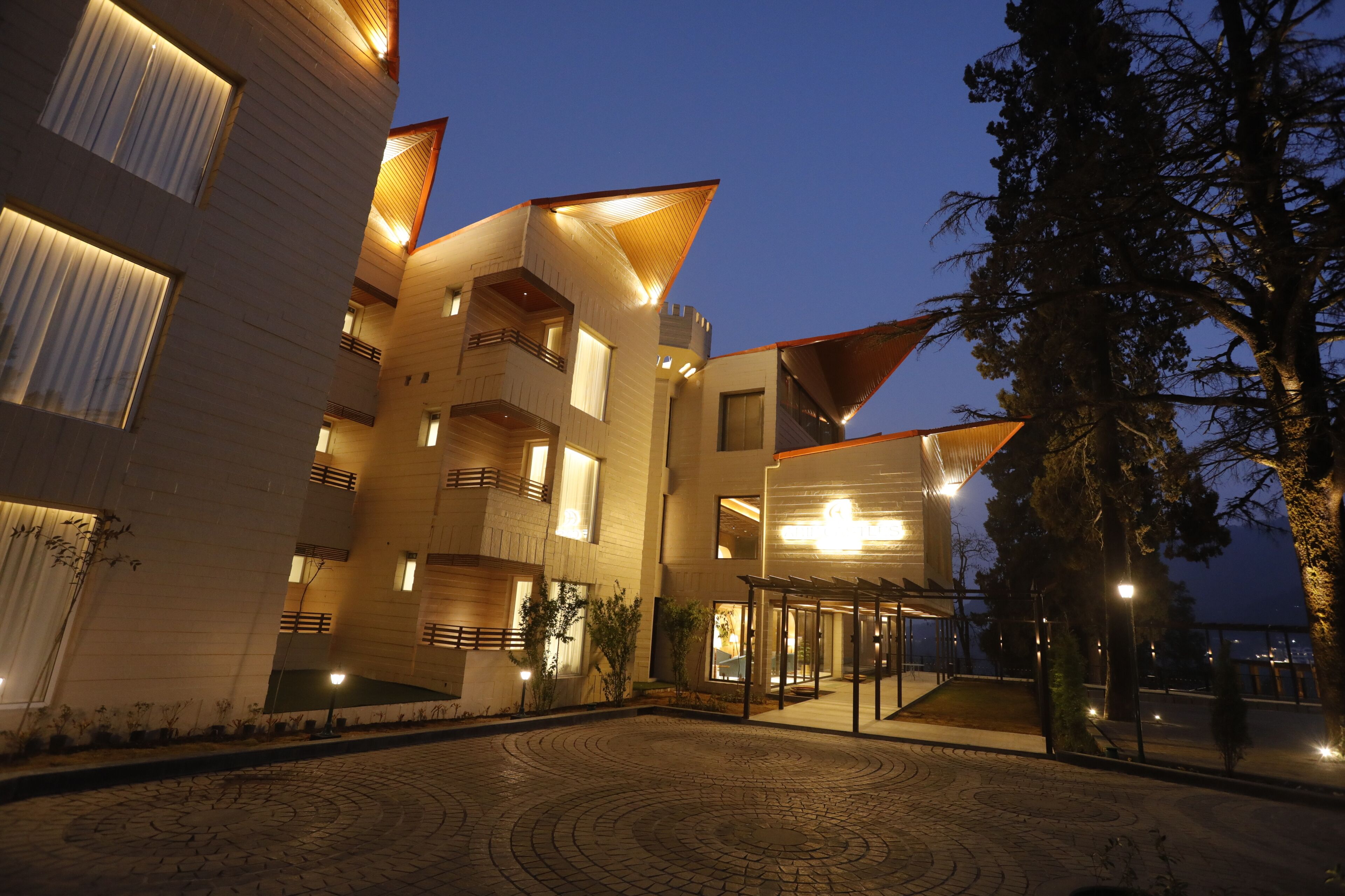A modern building with multiple balconies, a courtyard with patterned paving, and a well-lit entrance.