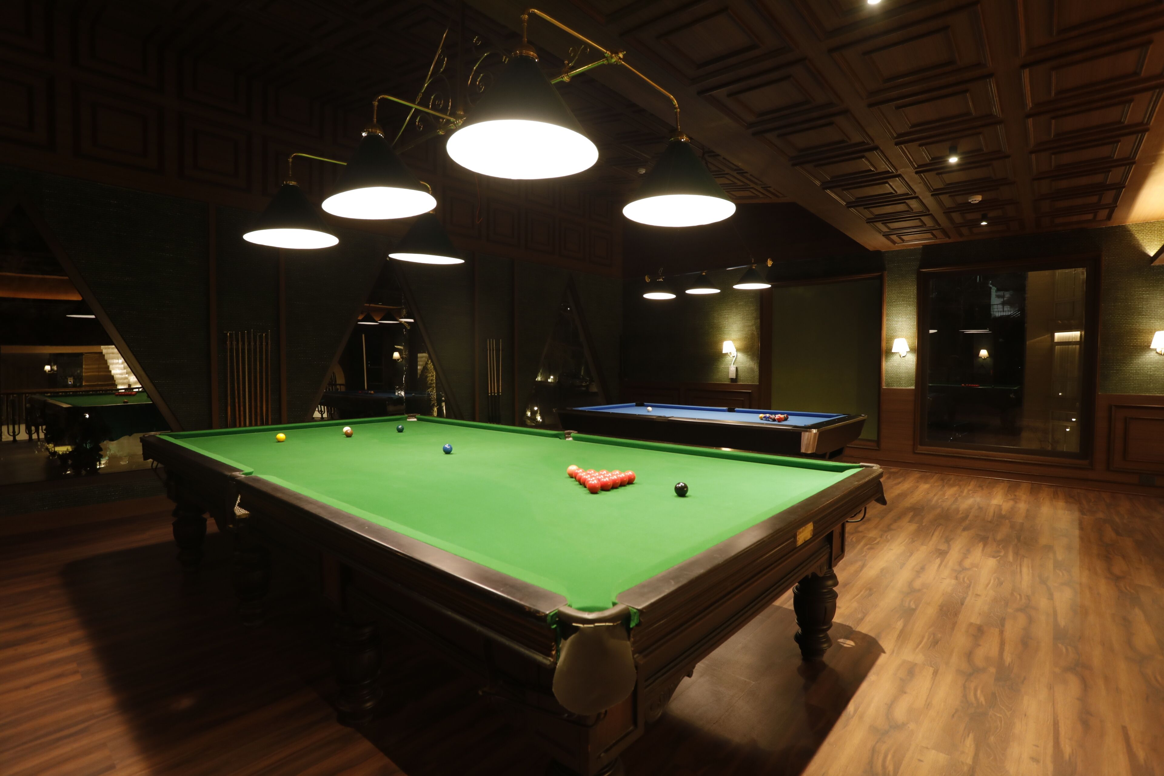A pool table with balls, overhead lighting, and a wooden floor.