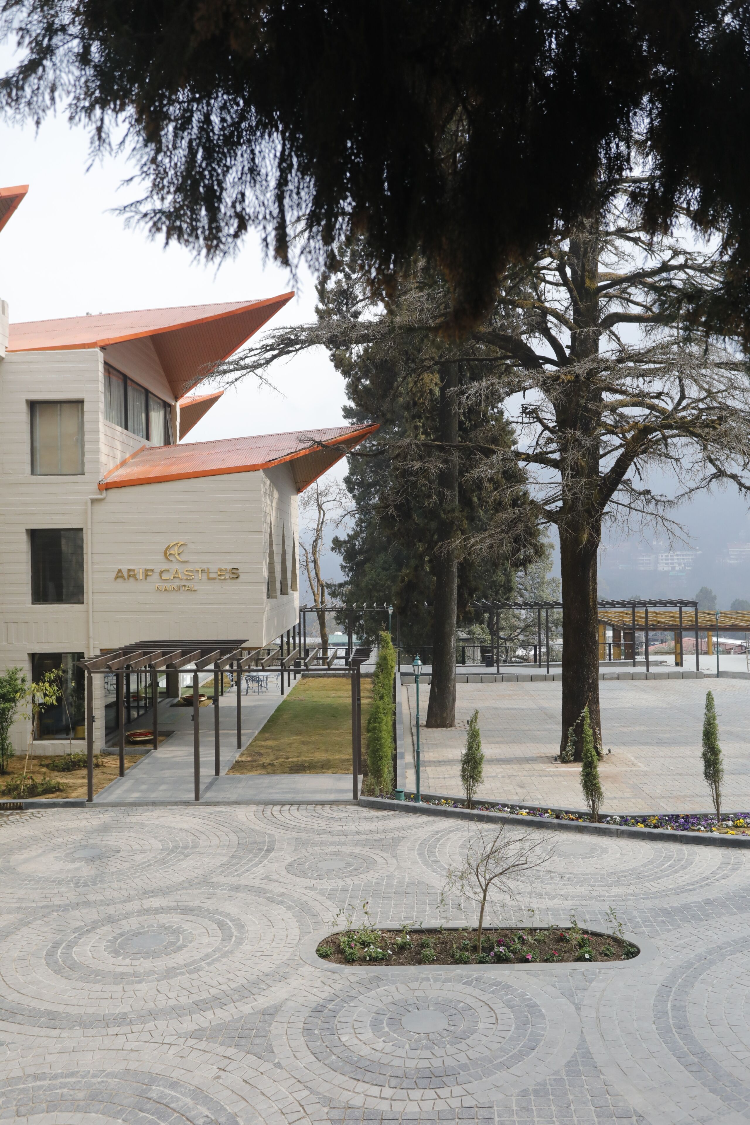 A building with the name 'ARF CASTLES' on the facade, a paved courtyard with a circular pattern, and a large tree in the foreground.