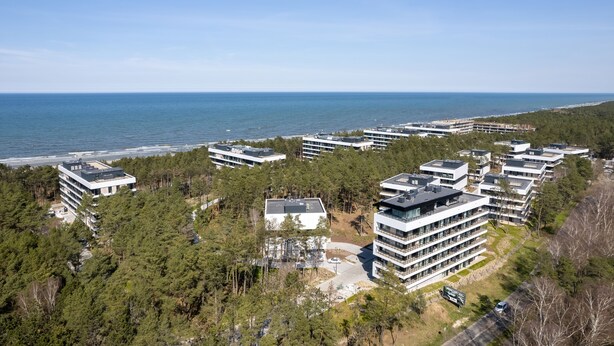 Een woongebied aan de kust met moderne appartementencomplexen, weelderige begroeiing en uitzicht op zee.