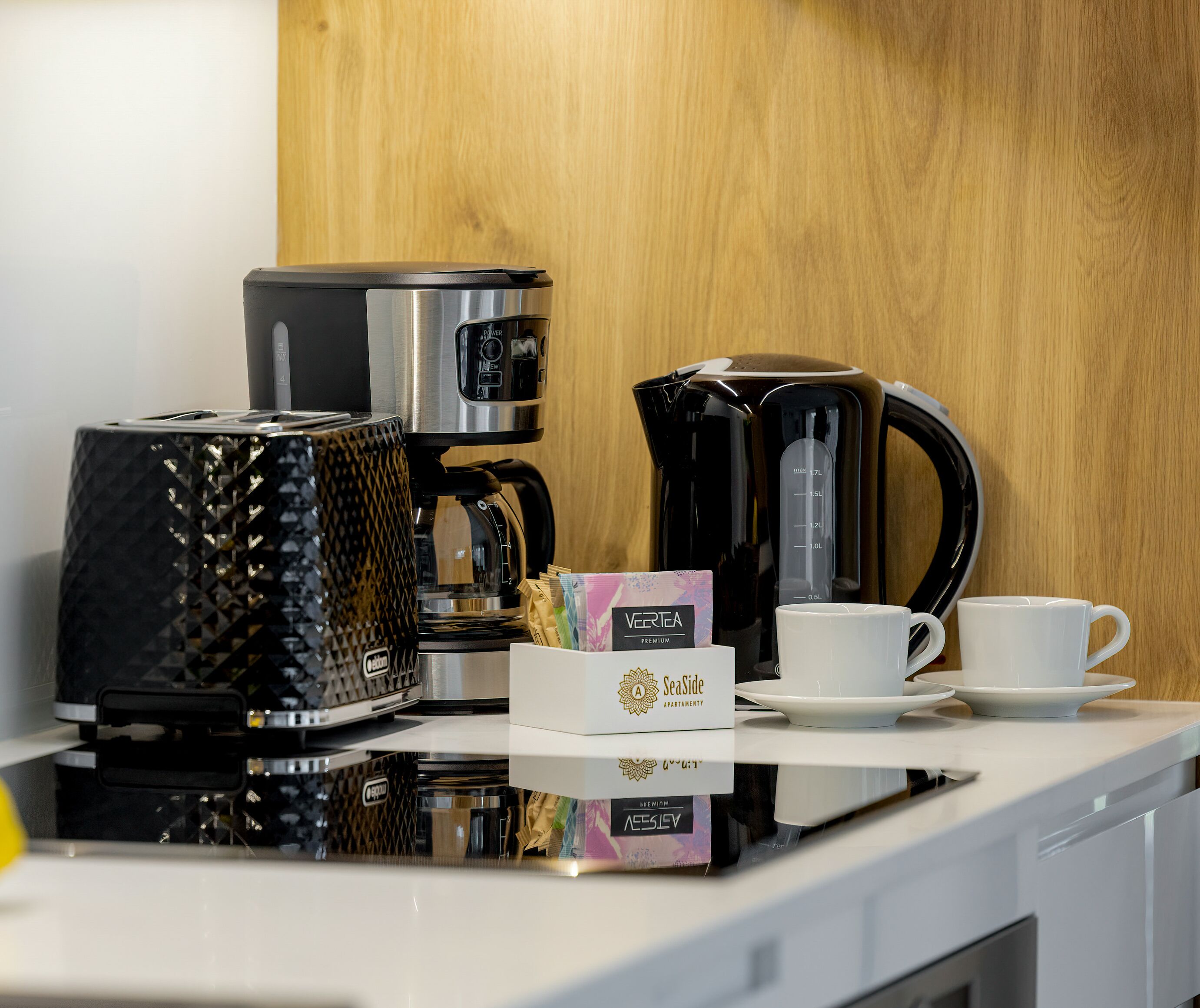 Eine Kaffeemaschine, ein Wasserkocher, eine Kapselbox und eine Tasse auf einer Arbeitsplatte.