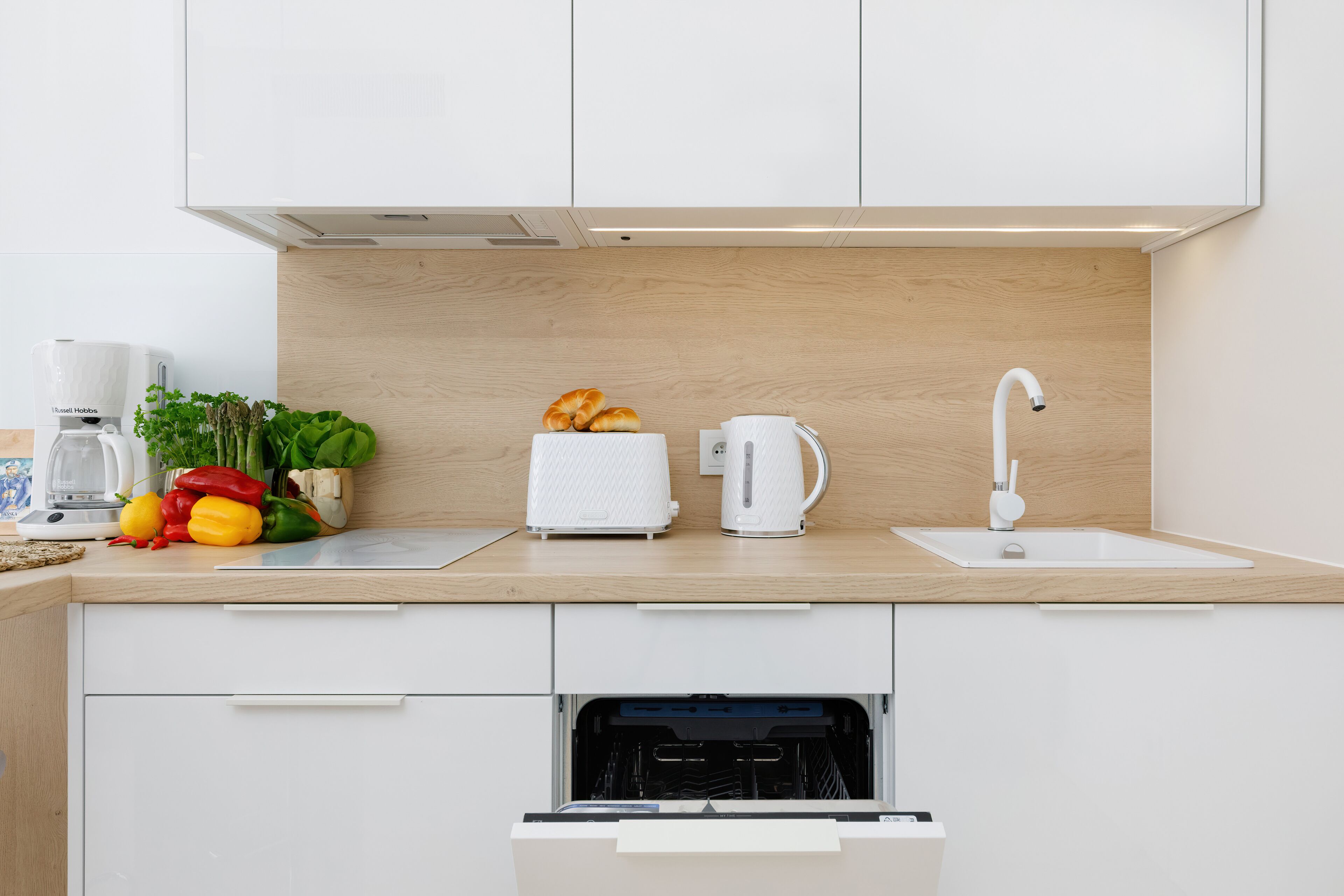 Una cocina moderna con armarios blancos, encimera de madera, lavavajillas integrado y un fregadero.