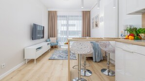 Een moderne keuken met witte kasten, een eethoek met een barkruk, en een woonkamer met een bank en televisie.