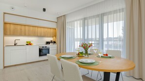 Een moderne keuken met witte kasten, een inbouwoven en een eethoek met een ronde tafel gedekt voor twee personen.