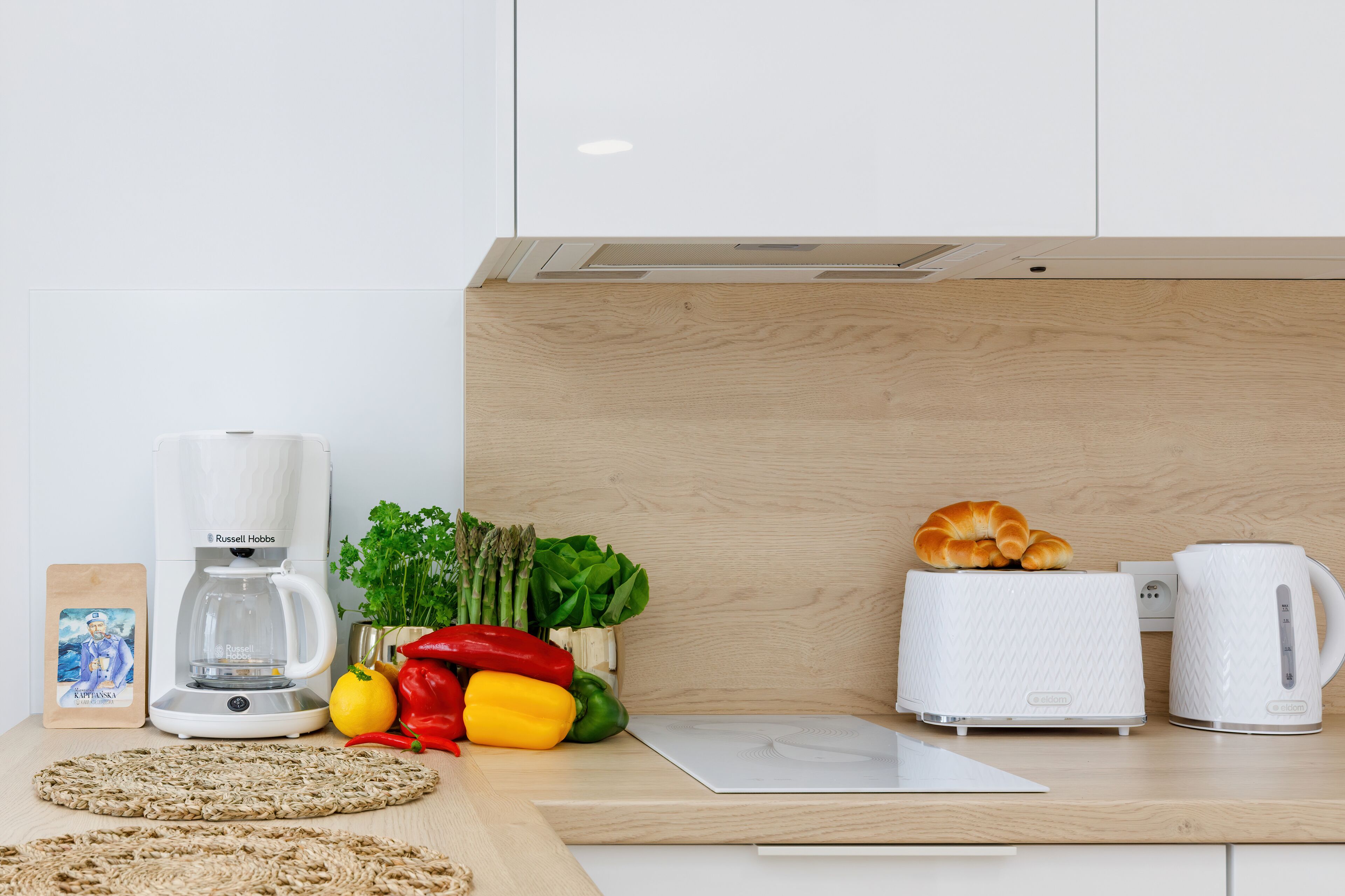 A kitchen counter with a coffee maker, toaster, kettle, and fresh vegetables.