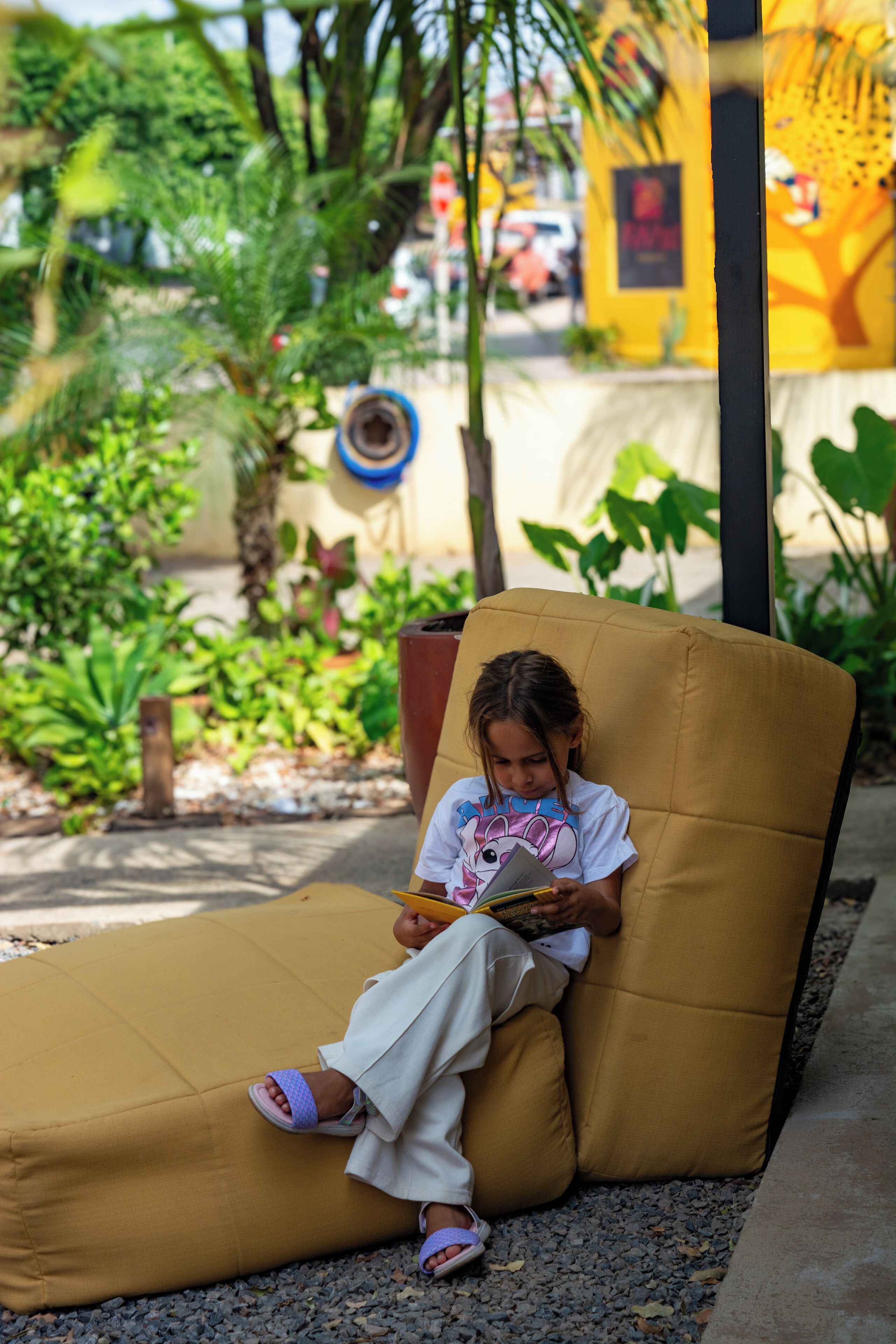 Un niño sentado en un banco amarillo acolchado al aire libre, leyendo un libro.