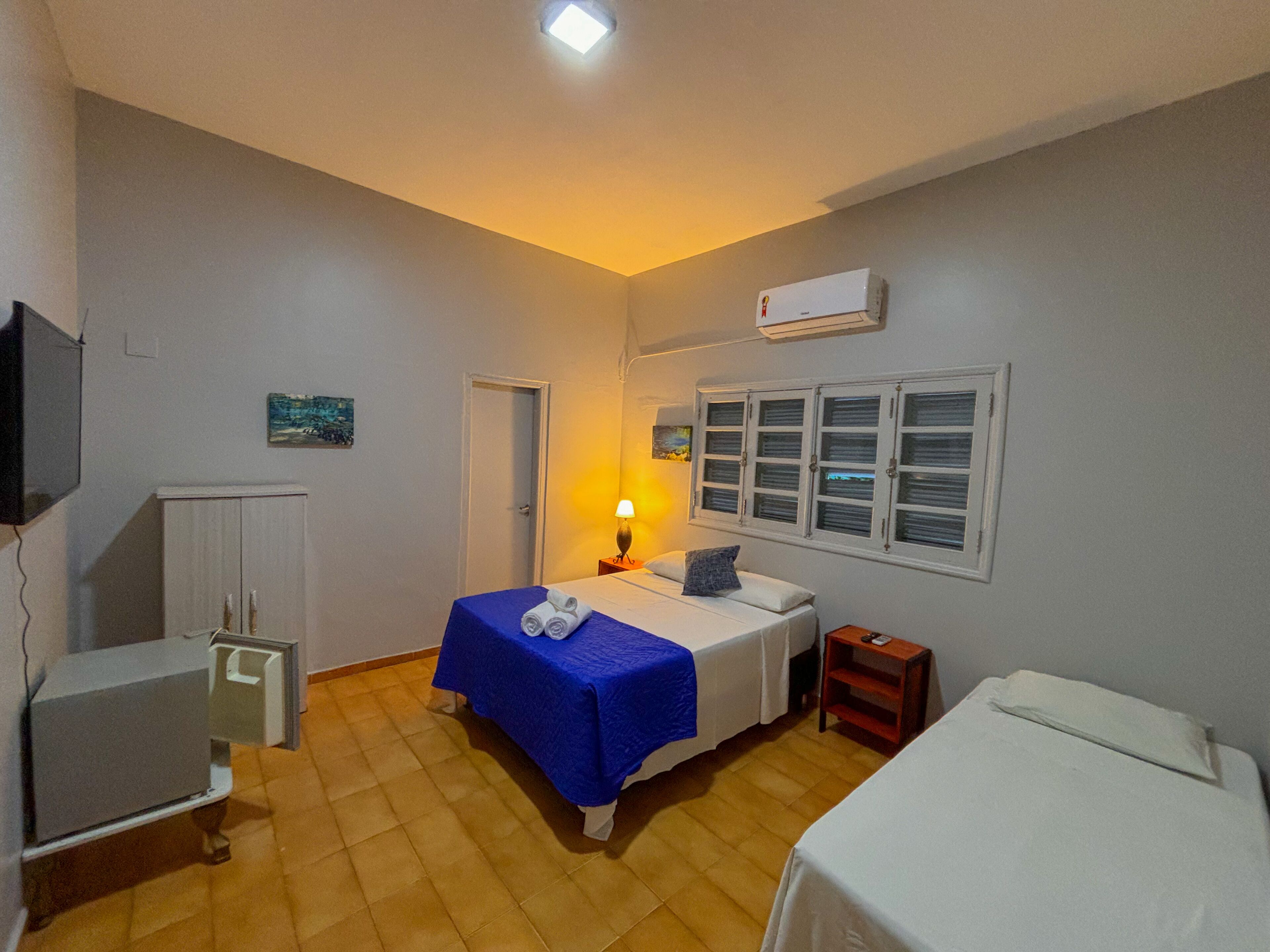Une chambre d’hôtel équipée d’un lit, d’un bureau, d’une chaise, d’une télévision, d’une fenêtre et d’un appareil de climatisation.