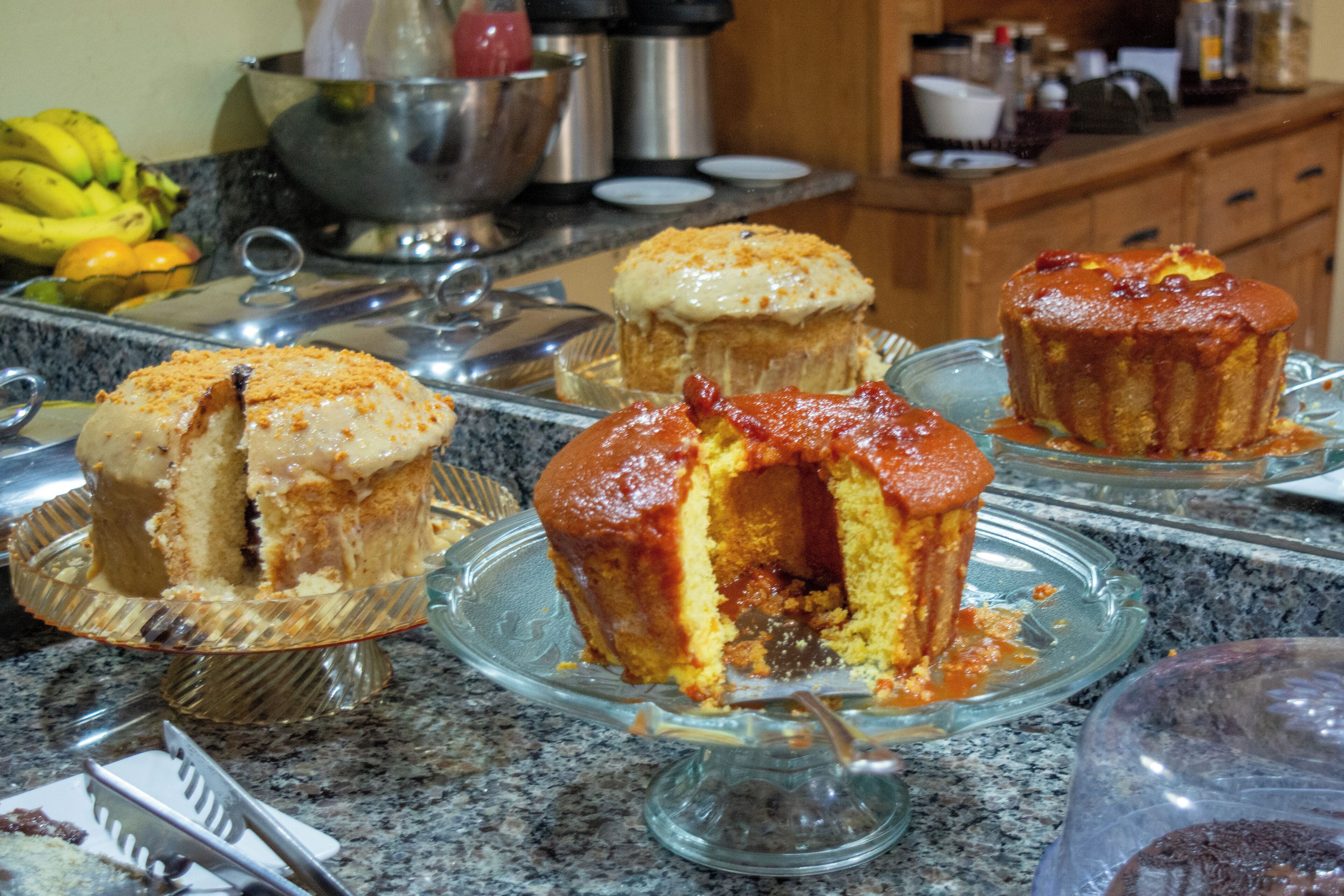A kitchen counter with various baked goods, including muffins and a cake, on glass stands.