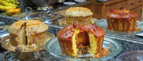 A kitchen counter with various baked goods, including muffins and a cake, on glass stands.