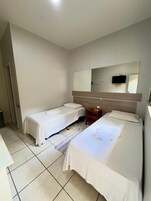 Habitación de hotel con dos camas individuales, cabecera de madera, mesita de noche de madera, un espejo y un televisor montado en la pared.