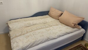 A bed with a beige patterned bedspread and two pillows, a blue headboard, and a small rug on the floor. - Ferienwohnung auf dem Bauernhof, Idyllisch am Stadtrand von Kaufbeuren (Kaufbeuren)