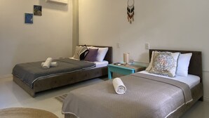 Une chambre d’hôtel moderne avec deux lits, une petite table et un attrape-rêves accroché au mur.