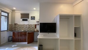 Une cuisine moderne équipée d’un four encastré, d’un évier et d’une fenêtre. Un téléviseur à écran plat est fixé au mur, au-dessus d’une étagère blanche.