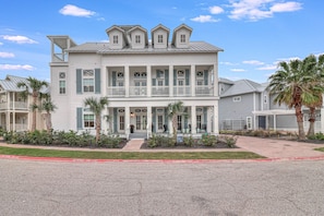 A two-story building with a balcony on the second floor, surrounded by palm trees and a landscaped garden. - A Southern Belle on the Texas Coast with lake views w/access to 20+ amenities (Port Aransas)