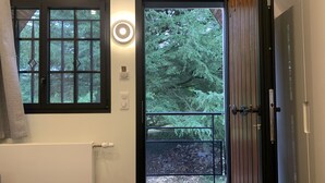 Bagno con finestra, un asciugamano, un interruttore della luce e una porta che dà su un’area esterna con vista sugli alberi.