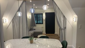 Zona pranzo con tavolo in marmo, sedie verdi e lampade a sospensione.