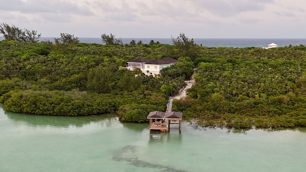 A secluded house surrounded by dense tropical vegetation, a small dock, and a clear view of the ocean.