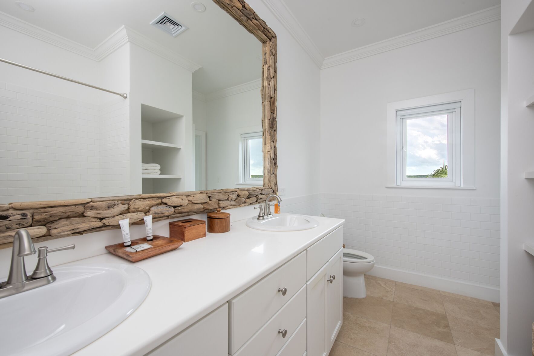 A bathroom with white tiles, a stone accent wall, a large mirror, and a window.