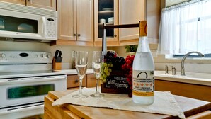 A kitchen with a microwave, stove, and wine tasting setup including a bottle, glasses, and a fruit basket. - Beachfront Bliss with Gulf Views & Heated Pool (Holmes Beach)