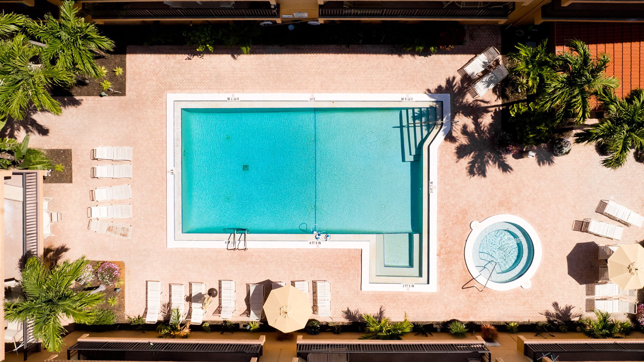 Vista aérea de una piscina rectangular con sillas de descanso cercanas y un pequeño jacuzzi circular.
