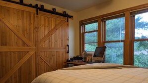 A bedroom with a large wooden wardrobe, a bed with a plaid bedspread, a desk with a computer, and a window with a view of trees. - Incredible MTN Views | In-Town | Pool | Hot Tub (Durango)