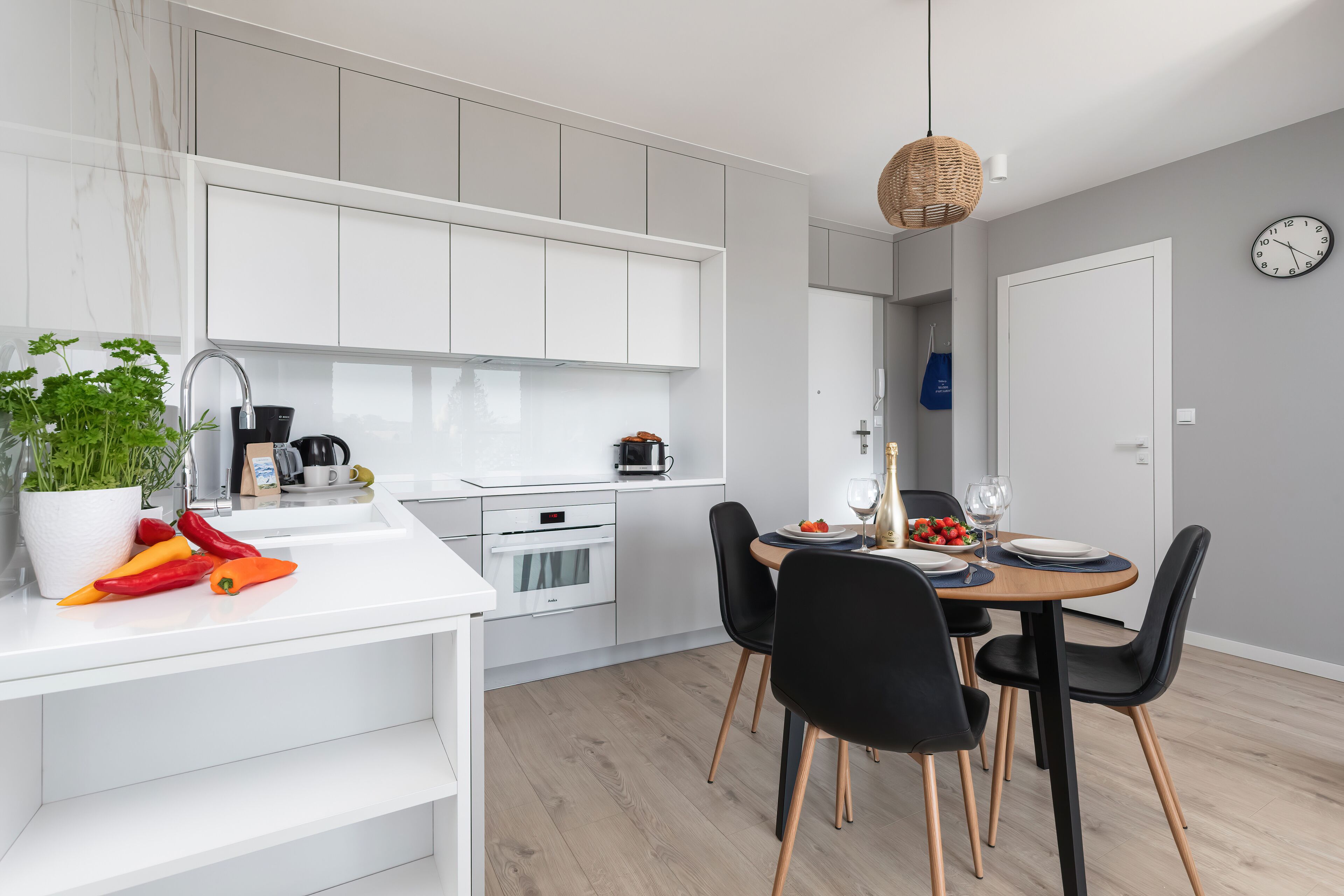 A modern kitchen with white cabinets, a built-in oven, and a dining area with black chairs and a wooden table.