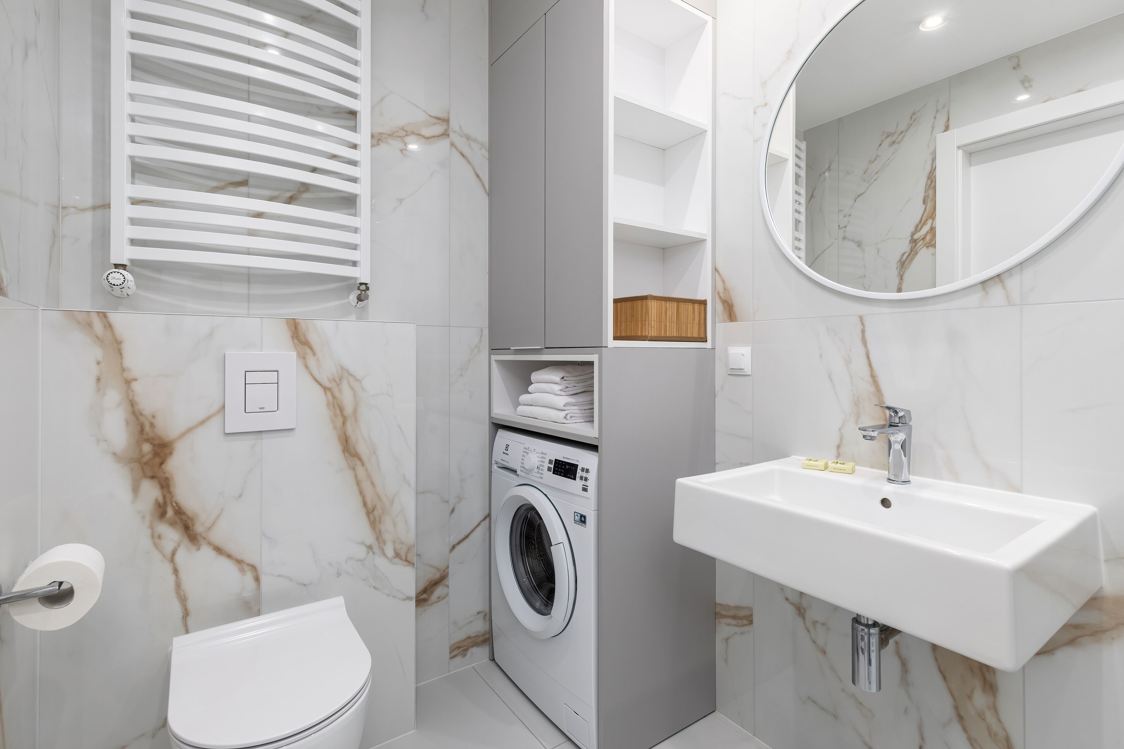 A modern bathroom with a built-in washing machine, a toilet, and a sink with a marble backsplash.