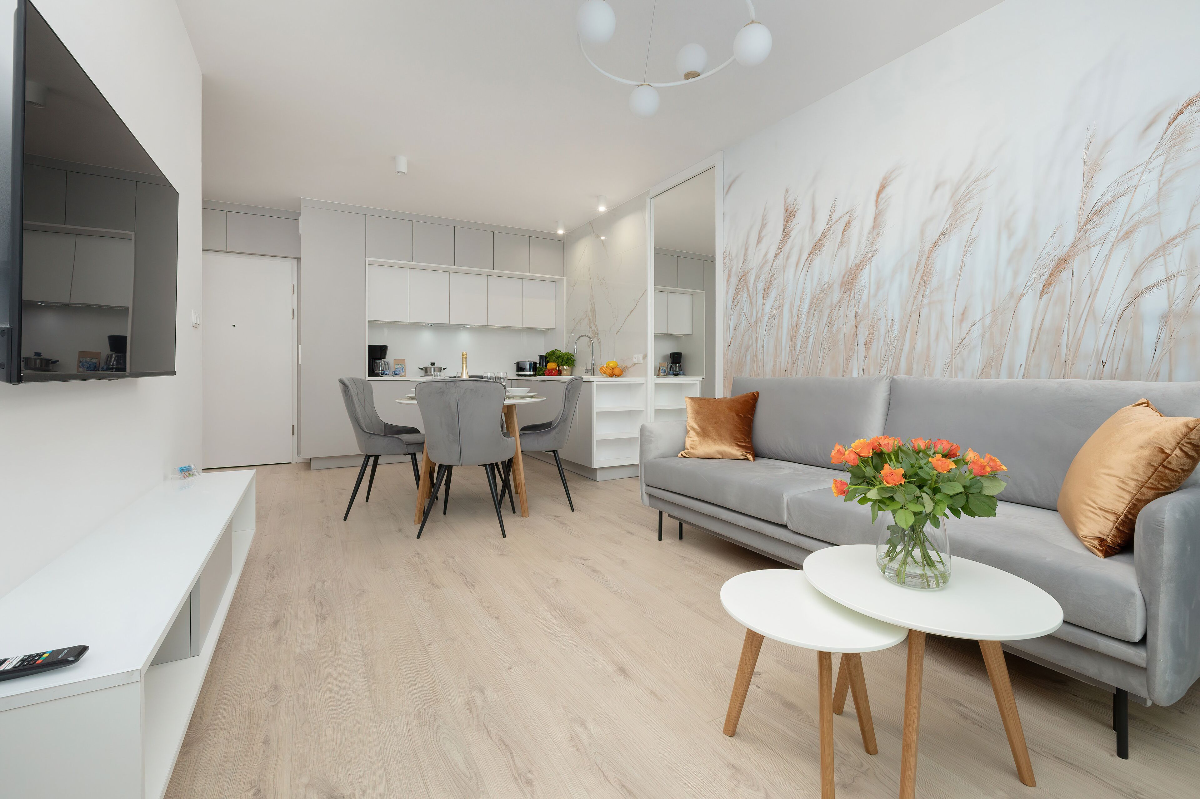 A modern living room with a grey sofa, a white coffee table, and a dining area with grey chairs.