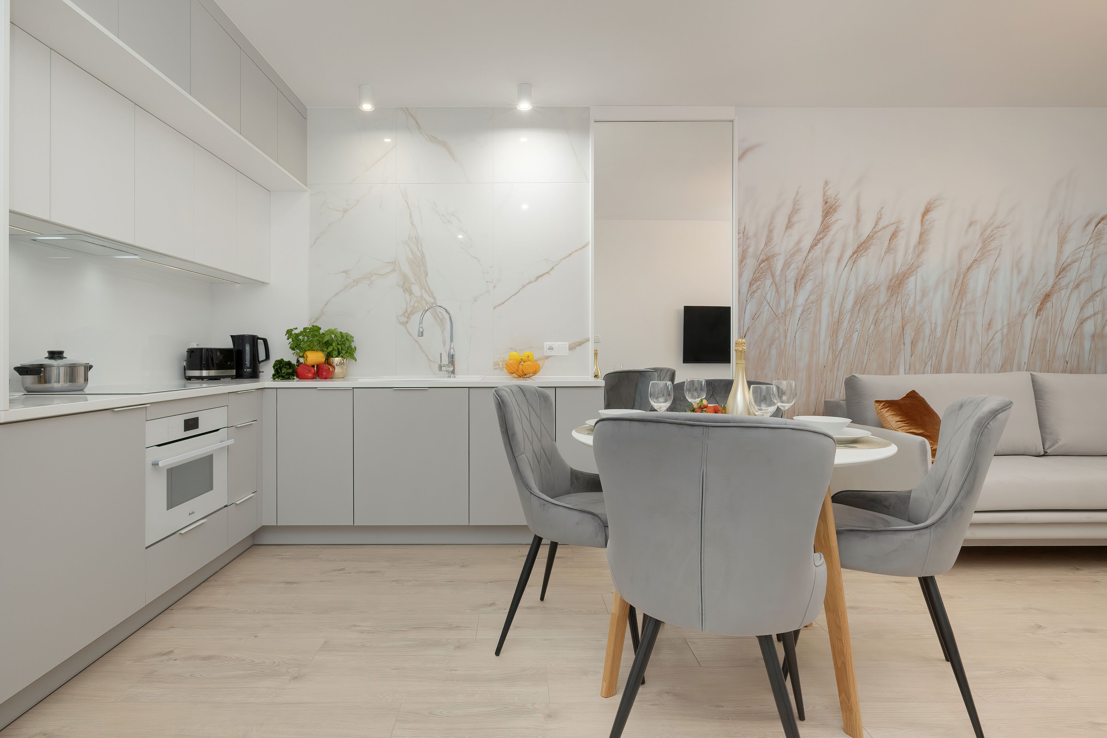 Une cuisine moderne avec des meubles blancs, un pare-feu en marbre et un coin repas comprenant des chaises grises et une table blanche.