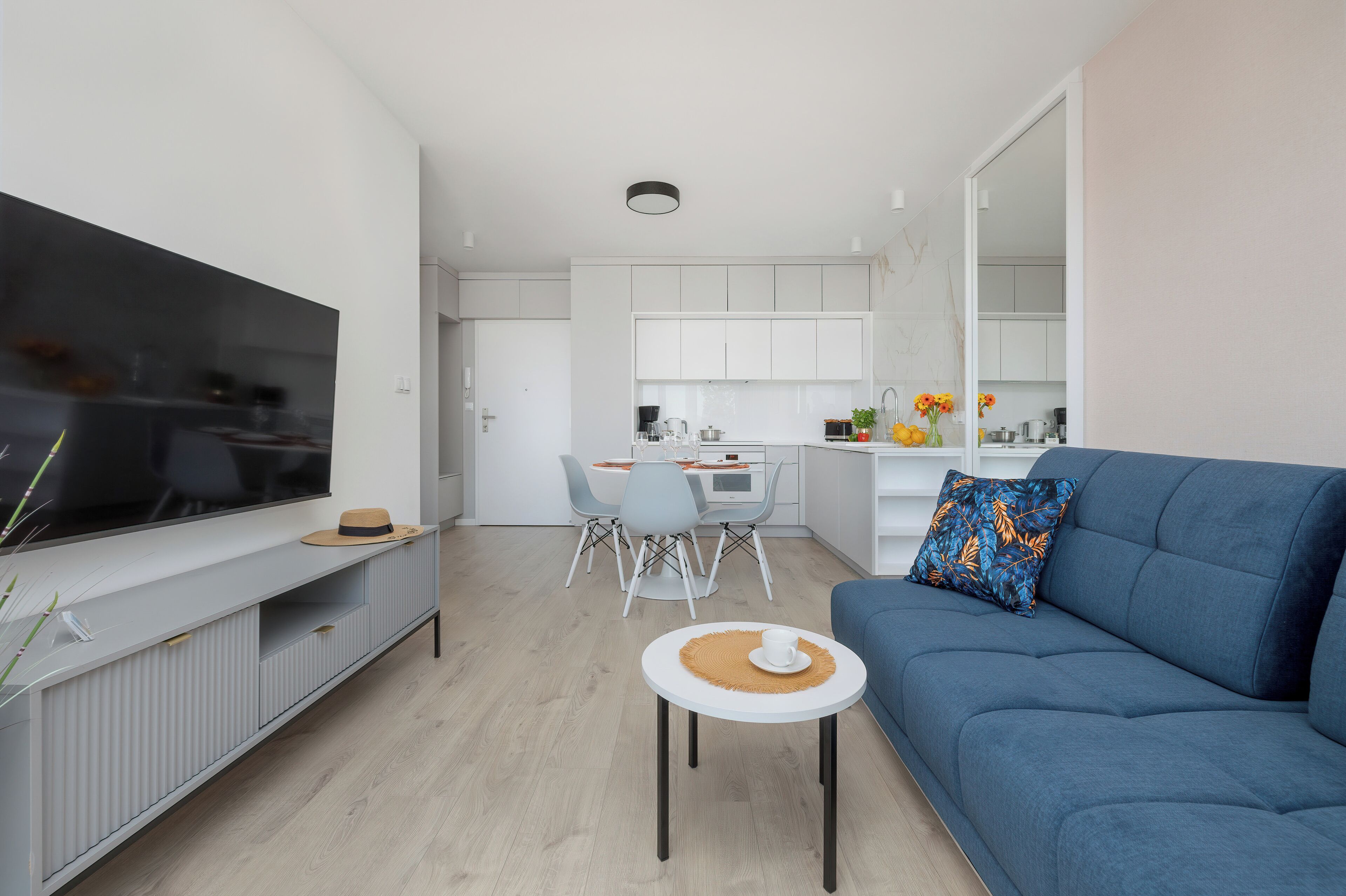 Una sala de estar moderna con televisor de pantalla plana, un sofá y una zona de comedor con sillas y una mesa.