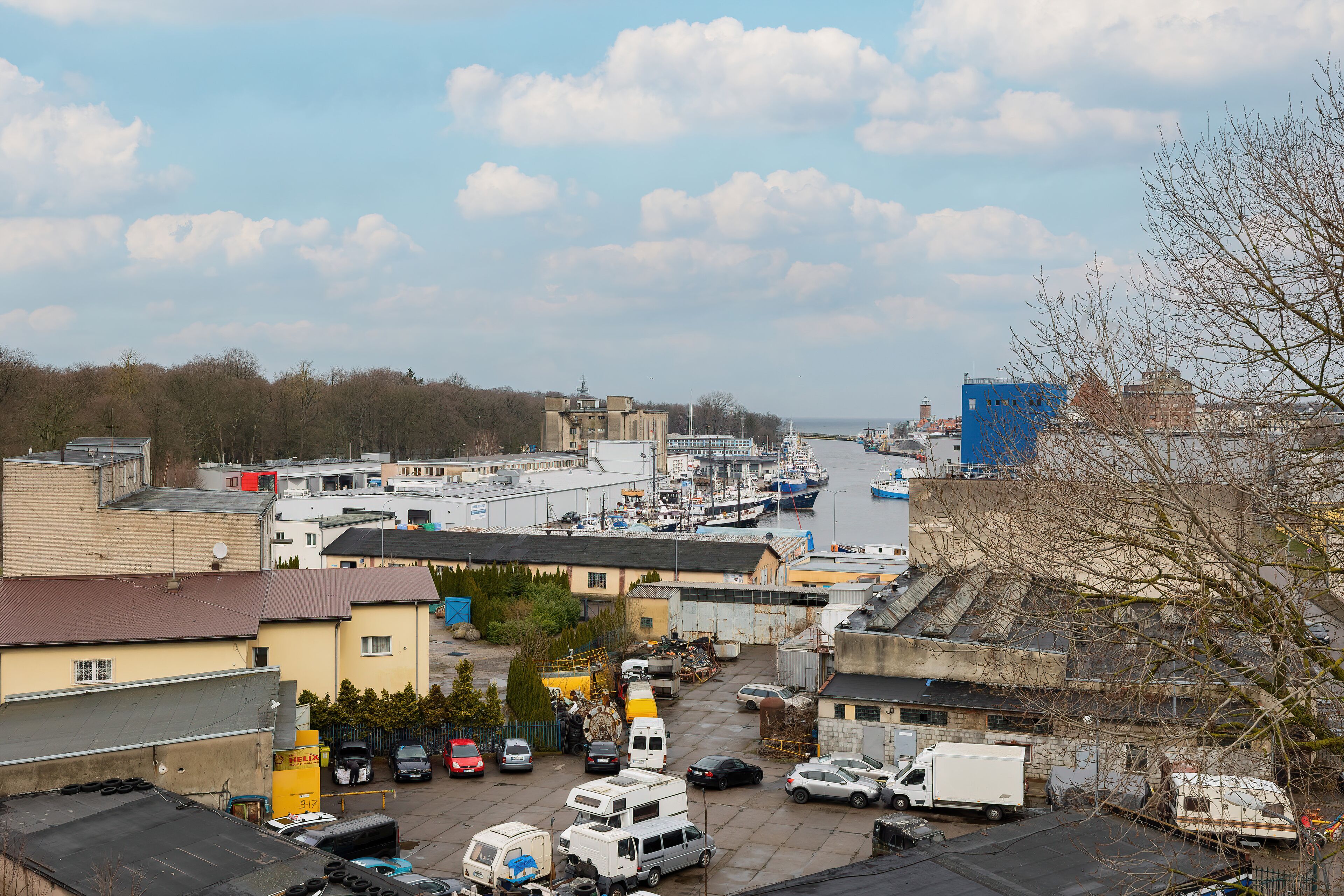A marina with boats docked, surrounded by buildings and a parking area with various vehicles.