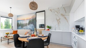 Una cocina moderna con armarios blancos, salpicadero de mármol y una zona de comedor con una mesa preparada para dos personas.