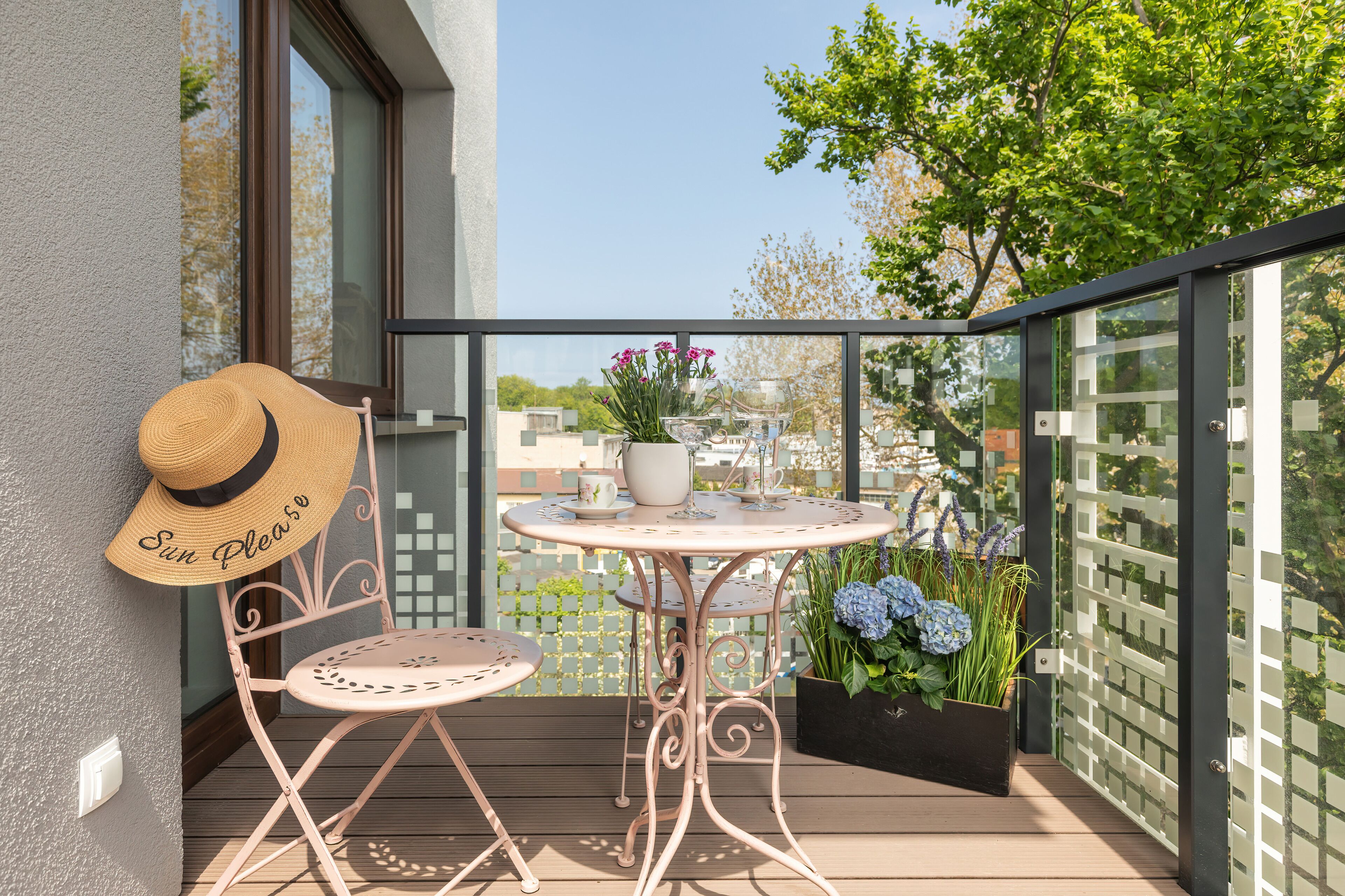 Un balcon avec une table et des chaises, un chapeau de soleil, une plante en pot et une vue sur des immeubles et des arbres.